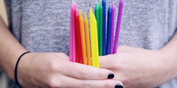 Two hands with black nail polish holding colorful candles.