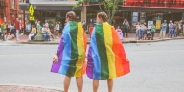 Two women standing with rainbow colored flags.