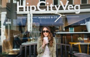 A woman sipping a drink outside a vegan restaurant.