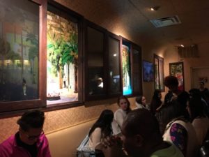 Customers are eating at the tables of a restaurant decorated with paintings on the wall.