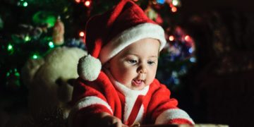 A baby wearing Santa Claus outfit near Christmas tree