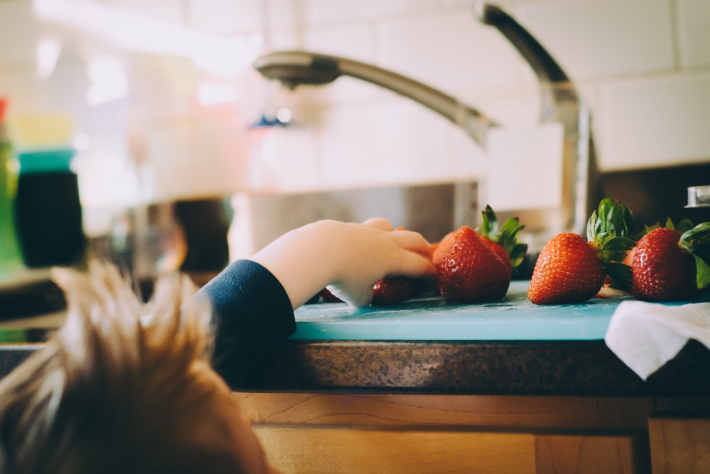 A child reaching strawberries on a kitchen countertop.