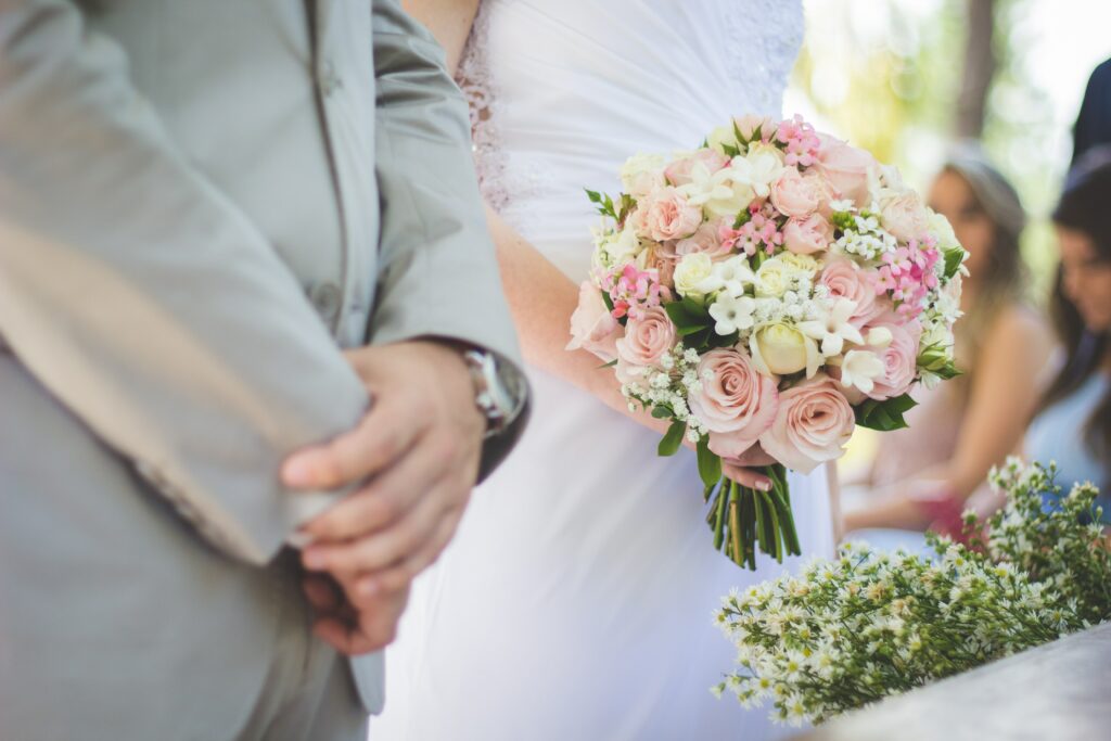 A bride holding flowers stands against the groom